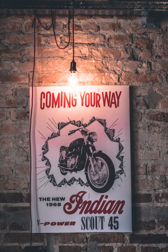 Retro 1968 Indian Scout 45 motorcycle poster with vintage bulb against brick wall.